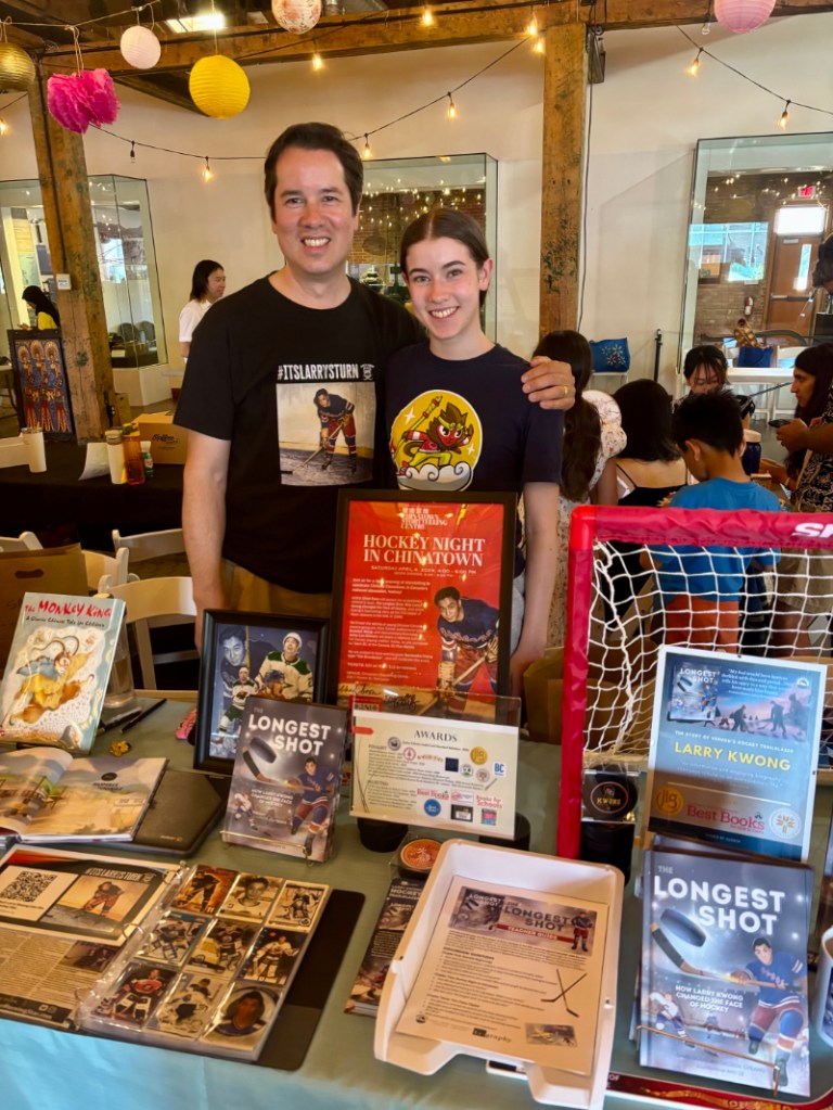 Vernon's Chad Soon (left), with daughter, Jasmine, promotes Vernon's  Larry Kwong's story at the 2025 Okanagan Asian Culture Festival on Aug. 30 in Kelowna. Soon co-authored the non-fiction children's book at centre of the photo, The Longest Shot: How Larry Kwong Changed the Face of Hockey, which has been shortlisted for two major Canadian literary awards.