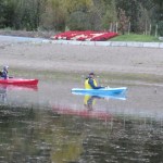 Two kayakers attempt to herd a pie-billed grebe trapped in plastic mesh to shore of Harrison Lake lagoon in hopes of freeing it.