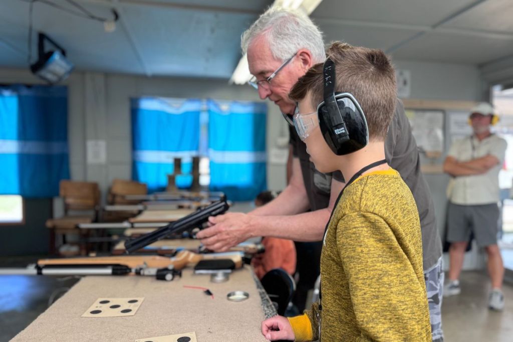 A young boy listens intently to instructions before handling and firing a rifle.