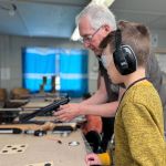 A young boy listens intently to instructions before handling and firing a rifle.