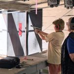 An NSRG coach is standing behind a young shooter.