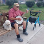 Herb Green sits on a bench and plays his banjo.