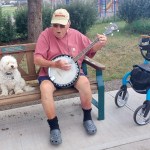 Herb Green sits on a bench and plays his banjo.